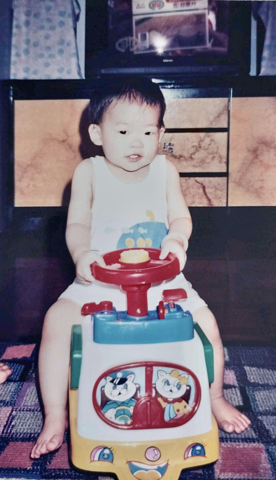 Emery as a toddler riding a colourful toy car