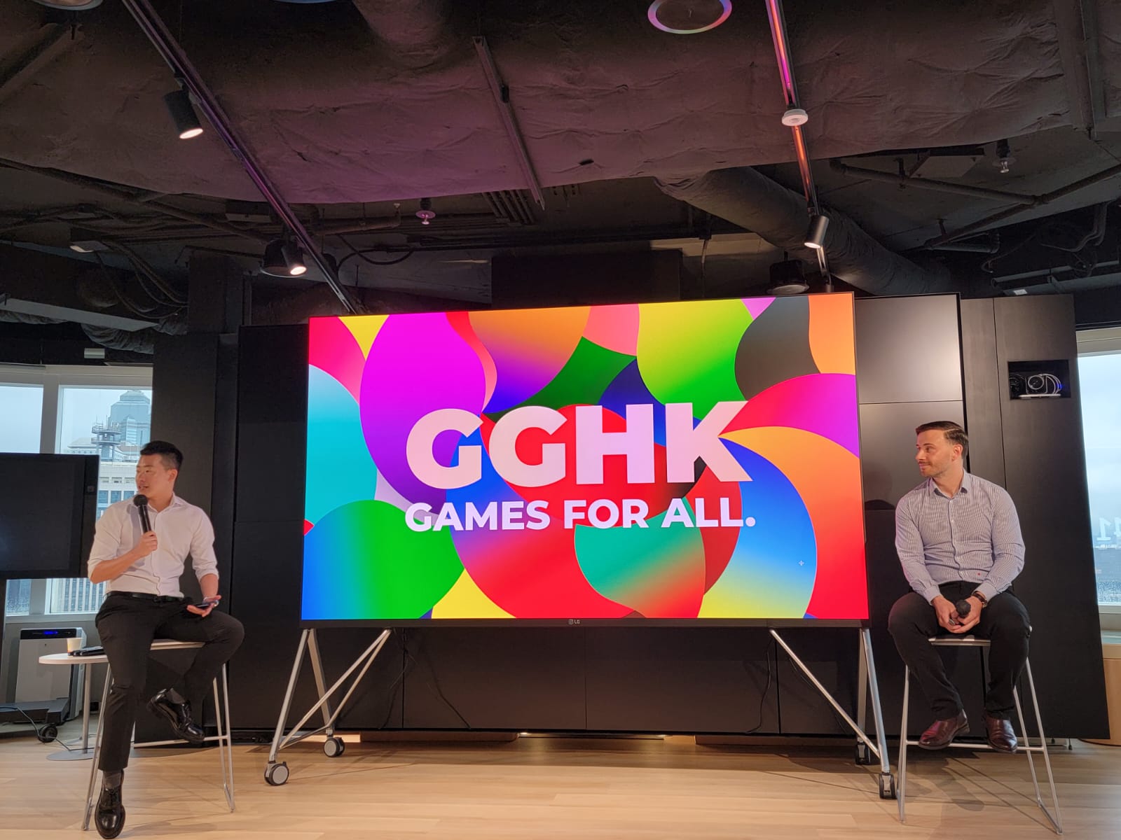 Two speakers seated on stage in front of a large Gay Games Hong Kong screen reading Games for all