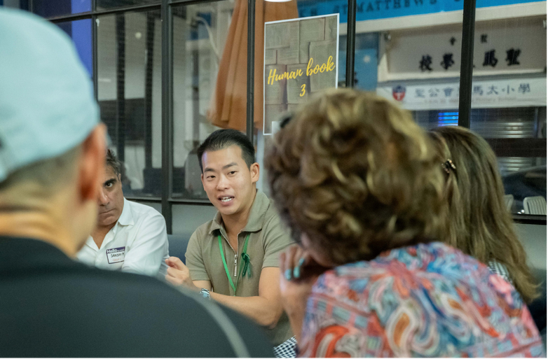 Emery speaking to a small circle of attendees seated around a table at a group conversation event
